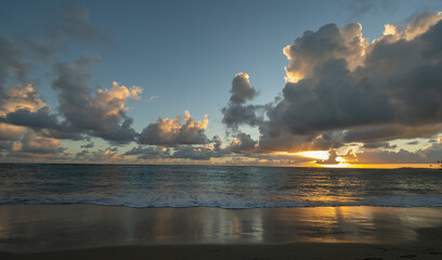 beach vacation sunset scenic suns sunrise reflection on the wet sand from waves receding Caribbean sea waves in the Dominican Republic sun setting behind clouds with golden glow in sky horizontal 