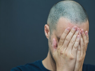 Fototapeta premium Sad and desperate man covers his face with his hands. Black color copy space