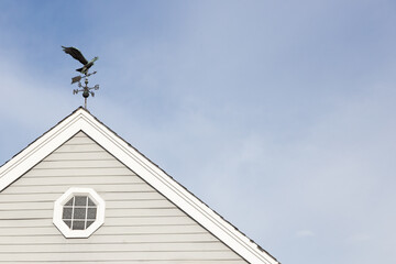 A weather vane on a white house roof on a blue sky background.