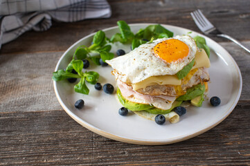Keto breakfast sandwich with fried eggs, ham, cheese, and avocado. Served with fresh blueberries and lamb´s lettuce