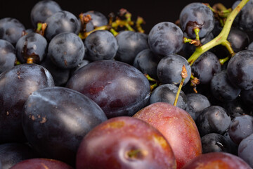 Purple fruits grapes and plums on white plate on black background