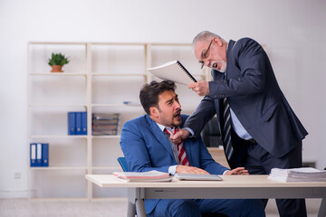 Old boss and young male employee in bullying concept