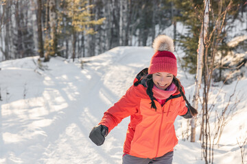 Fototapeta na wymiar Happy Asian woman laughing walking in snow forest during winter. Beautiful portrait of young adult smiling wearing cold weather hat and gloves, orange jacket.