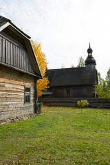 An old rustic wooden hut. In the background there is a rustic wooden church.