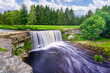 Large river waterfall falling down the cliff in a green forest landscape of northern Europe.