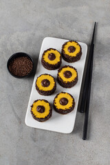 Sweet creamy pumpkin sushi rolls with chocolate sprinkles and filling on a ceramic plate on a light gray background top view