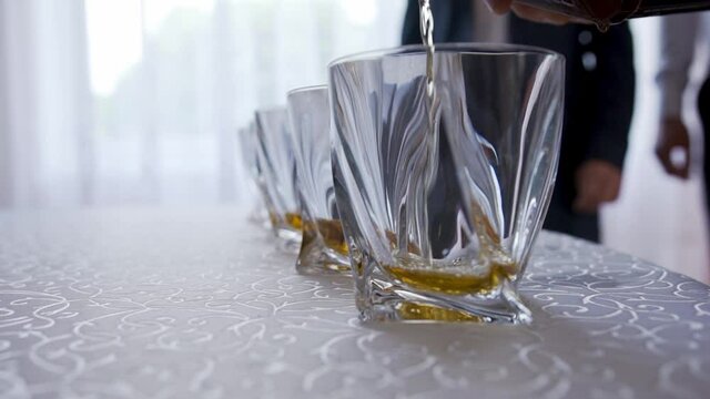 On the table are a row of clean square glasses and someone pours a brown drink of cognac or whiskey. The morning starts with alcohol. Relax with an expensive alcoholic beverage. Celebrating success