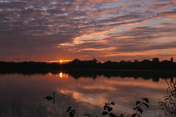 Dark sunset or sunrise of orange color above the horizon of a lake. Symmetry of dramatic sky in the water in rural scene.