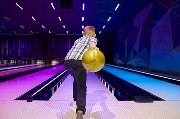 Boy holds a ball at the lane in bowling alley