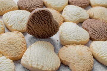 Lots of colorful heart-shaped cookies on a baking sheet, chocolate is on the edge