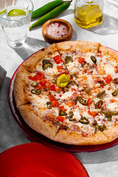 Spicy pizza with chicken, tomatoes and jalapenos on the light gray table vertical photo