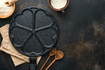 Empty frying pan black, skillet with stone nonstick coating for baking pancakes in shape of breakfast hearts and ingredients on gray concrete table background. Breakfast for Valentines Day. Top view.