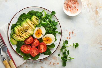 Avocado, cherry tomato, spinach and chicken egg, microgreens peas and black sesame seeds fresh salad in bowl on white stone table background. Healthy breakfast food concept. Top view.
