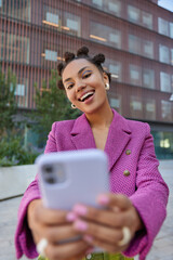Vertical shot of positive carefree teenage girl with teendy hairstyle dressed in pink jacket poses...