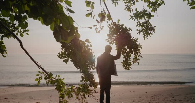 European Man in Leather Jacket Walks To The Shore To Observe The Sunrise in Knäbäckshusen Beach in South Sweden Skåne With Branches in Foreground, Static Wide Shot