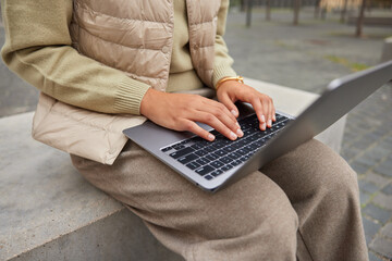 Cropped shot of unrecognizable female blogger types text publication on portable laptop computer...