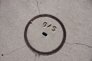 Close-up view of a small concrete and iron cover plate for a gas valve on a city street sidewalk