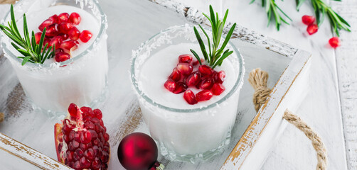 Christmas coconut punch with pomegranate seeds and sprigs of rosemary on light background. Selective focus. Top view