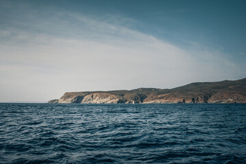 Seaside cliffs and sailboat with Calanans lighthouse next to Cadaques and S'Ocelleta headland, Catalonia, Spain.