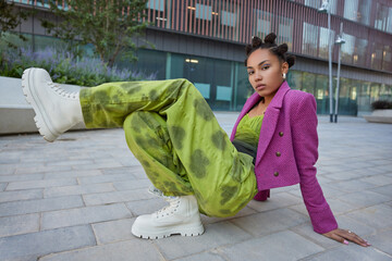 Horizontal shot of stylish teenage girl wears fashionable cloths and white boots has bright makeup...