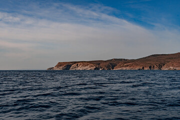 Seaside cliffs and sailboat with Calanans lighthouse next to Cadaques and S'Ocelleta headland, Catalonia, Spain.