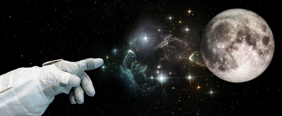 Astronauts hand points towards the moon in the starry sky. Moon and space exploration concept. Elements of this image furnished by NASA.