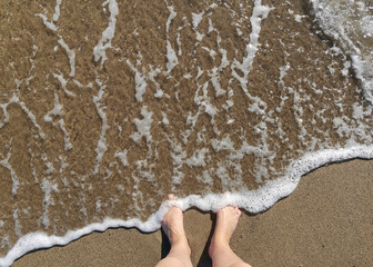 Bare feet and sea foam on a sandy beach. Top view
