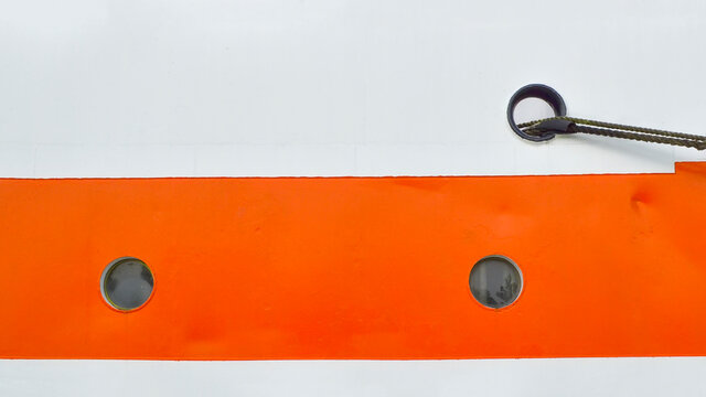 Close-up of two small portholes on the white-orange side of the ship