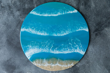 Resin art painting with blue sea waves and beach on gray background.
