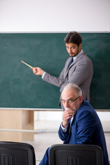 Young male employee and old boss in front of blackboard