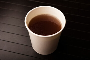 paper glass with delicious beef broth, dark background. Disposable tableware concept