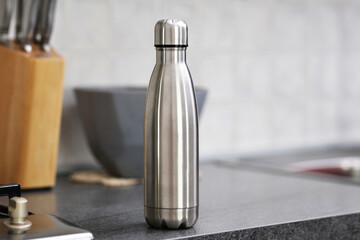 Stainless steel reusable water bottle on  interior of the apartment with a white kitchen in the...