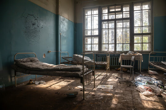 An old hospital room in an abandoned hospital. The beds are on a dirty floor. Shabby walls. Sunlight shines through the windows of an abandoned building.