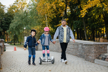 A father helps and teaches his young children to ride a Segway in the Park during sunset. Family...