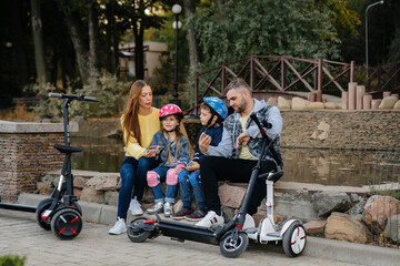 Fototapeta na wymiar A large happy family rides Segways and electric scooters in the Park on a warm autumn day during sunset. Family vacation in the Park.
