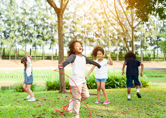 Group of diversity kids playing cheerful in the park. Children having fun and jumping with rope in the garden.