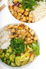Two vegan asian style bowls with fried tofu, rice, cucumbers, nut sauce seaweed and vegetables. Food sticks. Isolated on white, close up view.