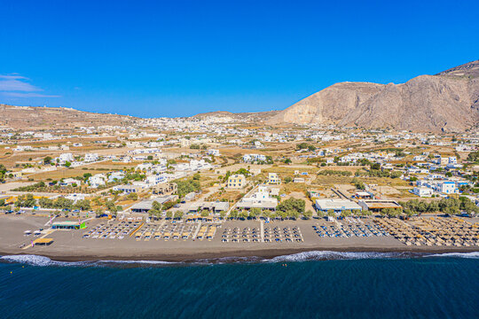 Top view aerial drone photo of black Perissa beach with beautiful turquoise water, sea waves and straw umbrellas. Vacation travel background. Aegean sea, Santorini Island, Greece