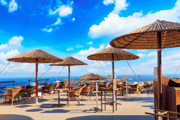 Restaurant with straw umbrellas in Oia village on Santorini island, Aegean sea, Greece.