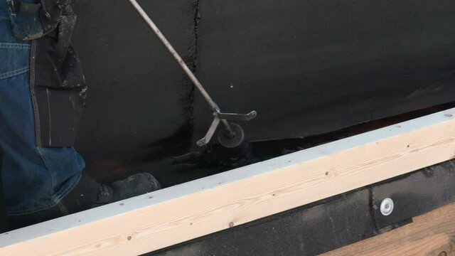 Roofer Laying tar paper with a flame thrower on a roof in Germany. You see flames and smoke.