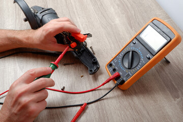 Power tool repair. A man repairs an angle grinder. Screwdriver, multimeter. Details of electrical...