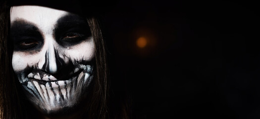 Young man wearing skull makeup in the dark. Halloween skeleton costume