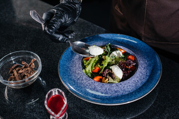 A professional chef prepares a delicious fresh salad of green vegetables and juicy veal in a modern and stylish restaurant. Cooking in a restaurant.
