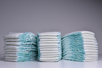 Tre stacks of baby disposable nappies over grey background. A large stacks of baby diapers, close-ups, diaper packaging.