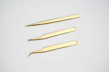 tools for eyelash extensions and eyebrow design. cosmetic tweezers in gold color on a white background