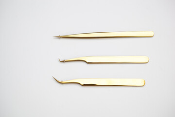 tools for eyelash extensions and eyebrow design. cosmetic tweezers in gold color on a white...