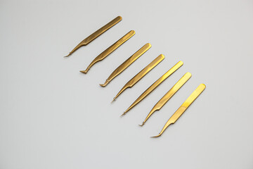 tools for eyelash extensions and eyebrow design. cosmetic tweezers in gold color on a white...