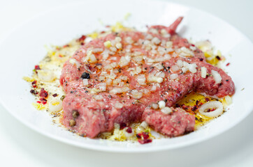 Minced meat with fresh spring onions and spices in the shape of a pig on the white plate, a creatively prepared burger in an interesting shape