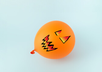 Orange balloon like pumpkin with drawn face on blue background.