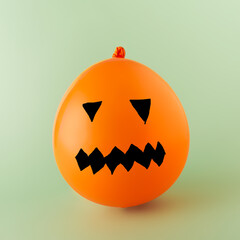 Orange balloon like pumpkin with drawn face on green background.